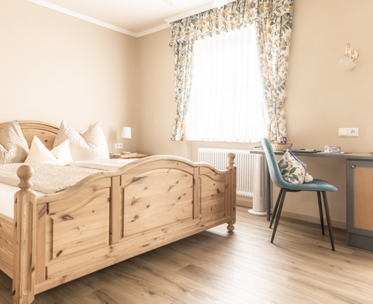 Gästeschlafzimmer im Bauernhof mit Holz-Doppelbett, Nachttisch und Schreibtischbereich am Fenster.