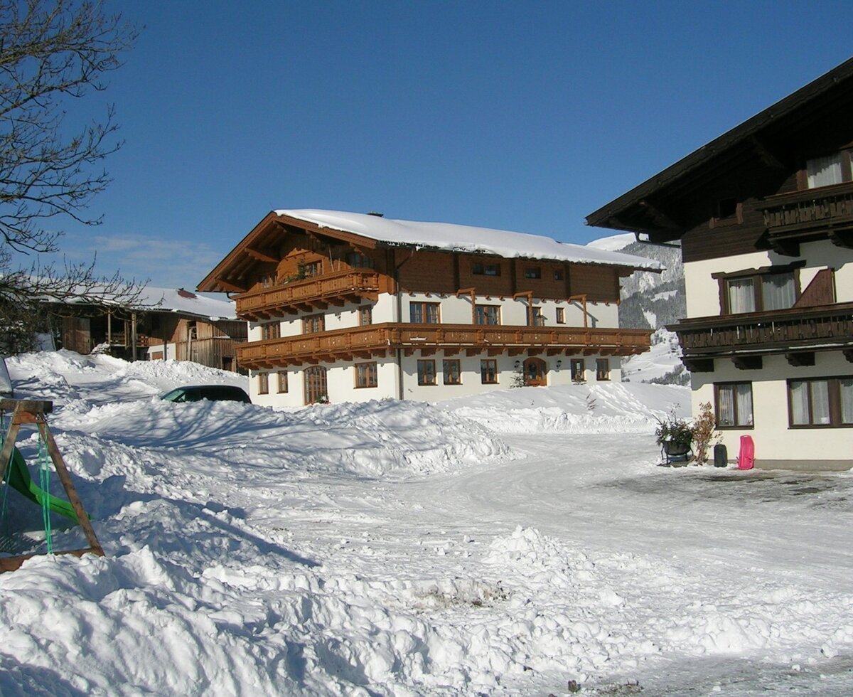 Außenansicht des Bauernhofs im Winter mit verschneiter Landschaft und traditionellen Holzfassaden.