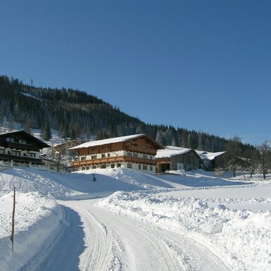 Zugang zum Bauernhof mit verschneiter Landschaft und Bergen im Hintergrund.