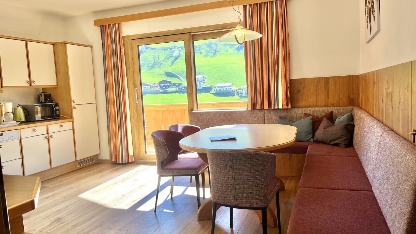 Offener Wohnbereich im Bauernhof mit voll ausgestatteter Küche, Essbereich mit Eckbank und Zugang zum Balkon mit Bergblick.