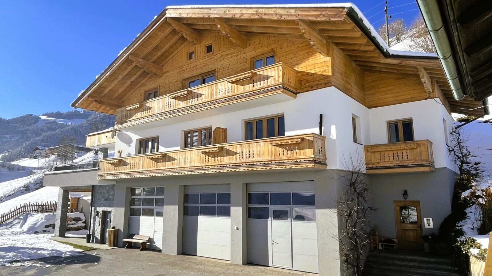 Außenansicht des Bauernhofs mit Holzbalkonen, weißer Fassade und Garagentoren, umgeben von Schnee.