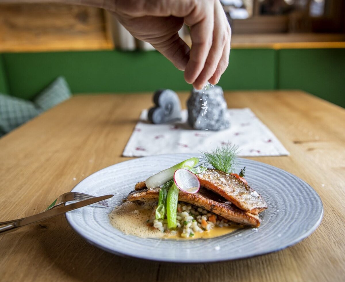 Ein Gericht mit gebratenem Fisch, Perlgraupen, Gemüse und Kräutern, serviert auf einem Holztisch im Bauernhof.