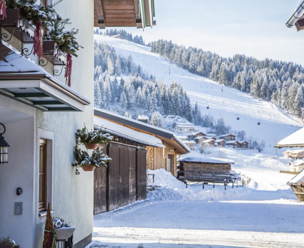 Außenbereich des Bauernhofs im Winter, mit Blick auf die schneebedeckte Skipiste und die umliegenden Berge.
