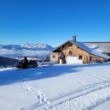 Die schneebedeckte Schoberhütte mit einem Schneemobil für den Wintertransfer und Blick auf den Untersberg.