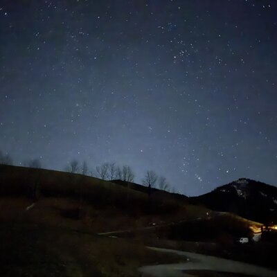 Der klare Sternenhimmel über der Almhütte, umgeben von dunklen Bergen und Hügeln in der Nacht.