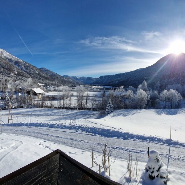 Sonniger Winterblick auf die schneebedeckte Landschaft mit Bergen und Tal vom Bauernhof.