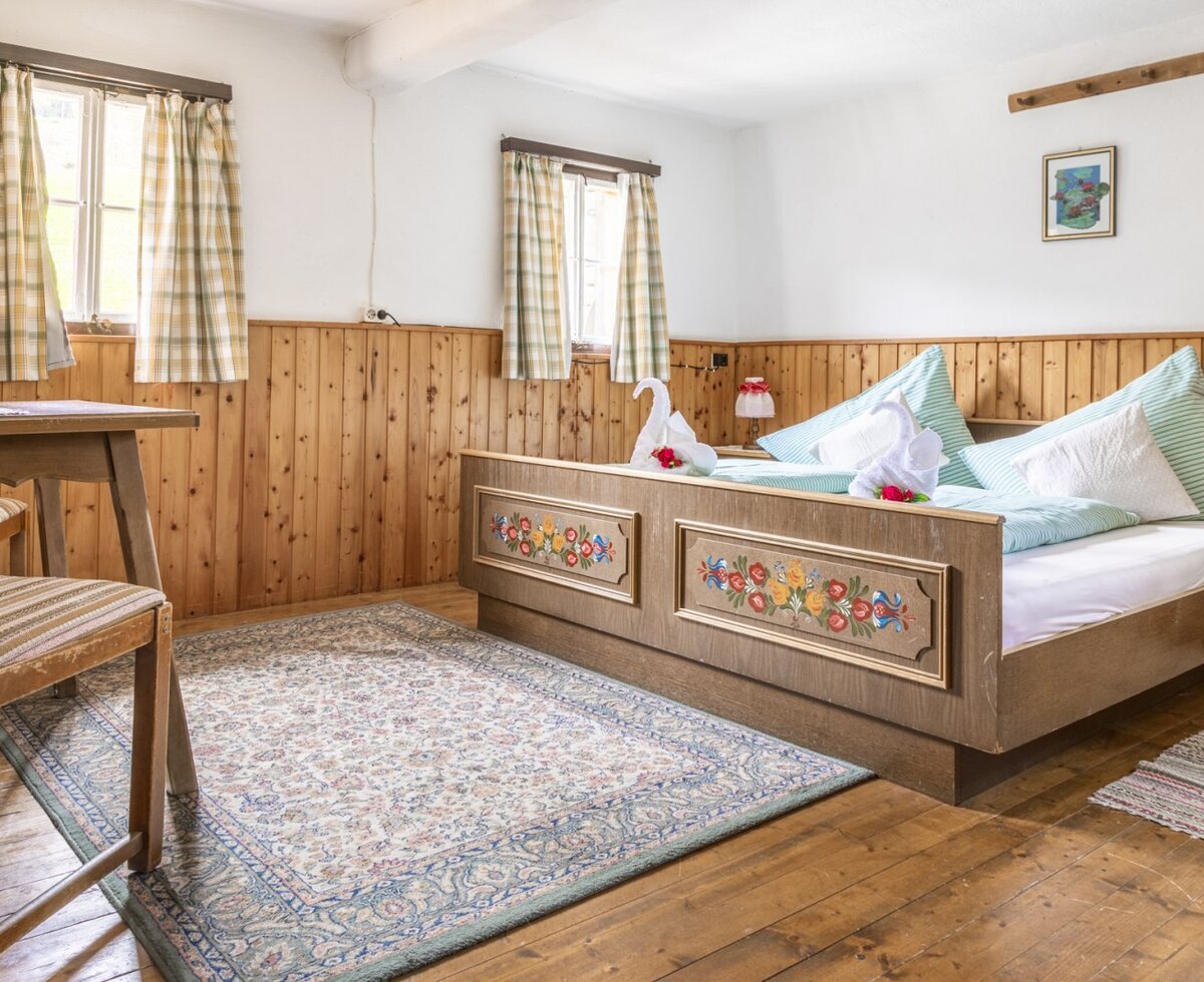 Schlafzimmer im Hof mit Doppelbett mit floralen Verzierungen, Holzvertäfelung und zwei Fenstern.
