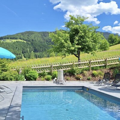 Außenpool des Hofes mit Sonnenliegen, Sonnenschirmen und Blick auf die bewaldeten Hügel.