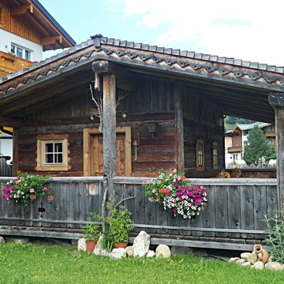 Ein traditionelles Holz-Nebengebäude auf dem Bauernhof mit überdachter Veranda und bunten Blumenkästen.