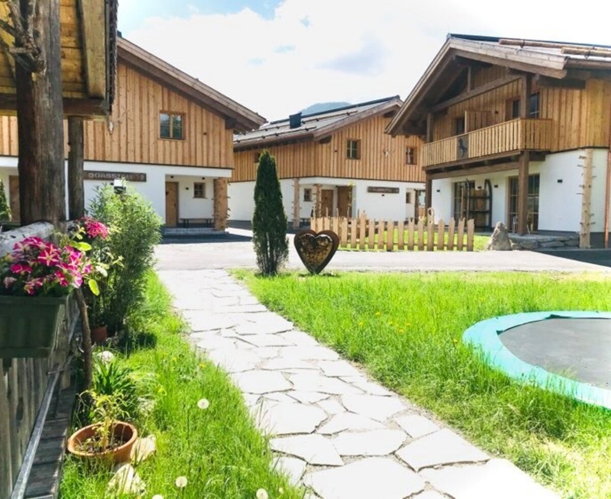 Außenansicht des Bauernhofs mit traditionellen Holzgebäuden, einem Garten und einem Trampolin.