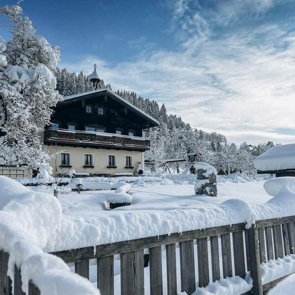 Der Bauernhof im Winter, umgeben von einer tief verschneiten Landschaft und Bäumen.