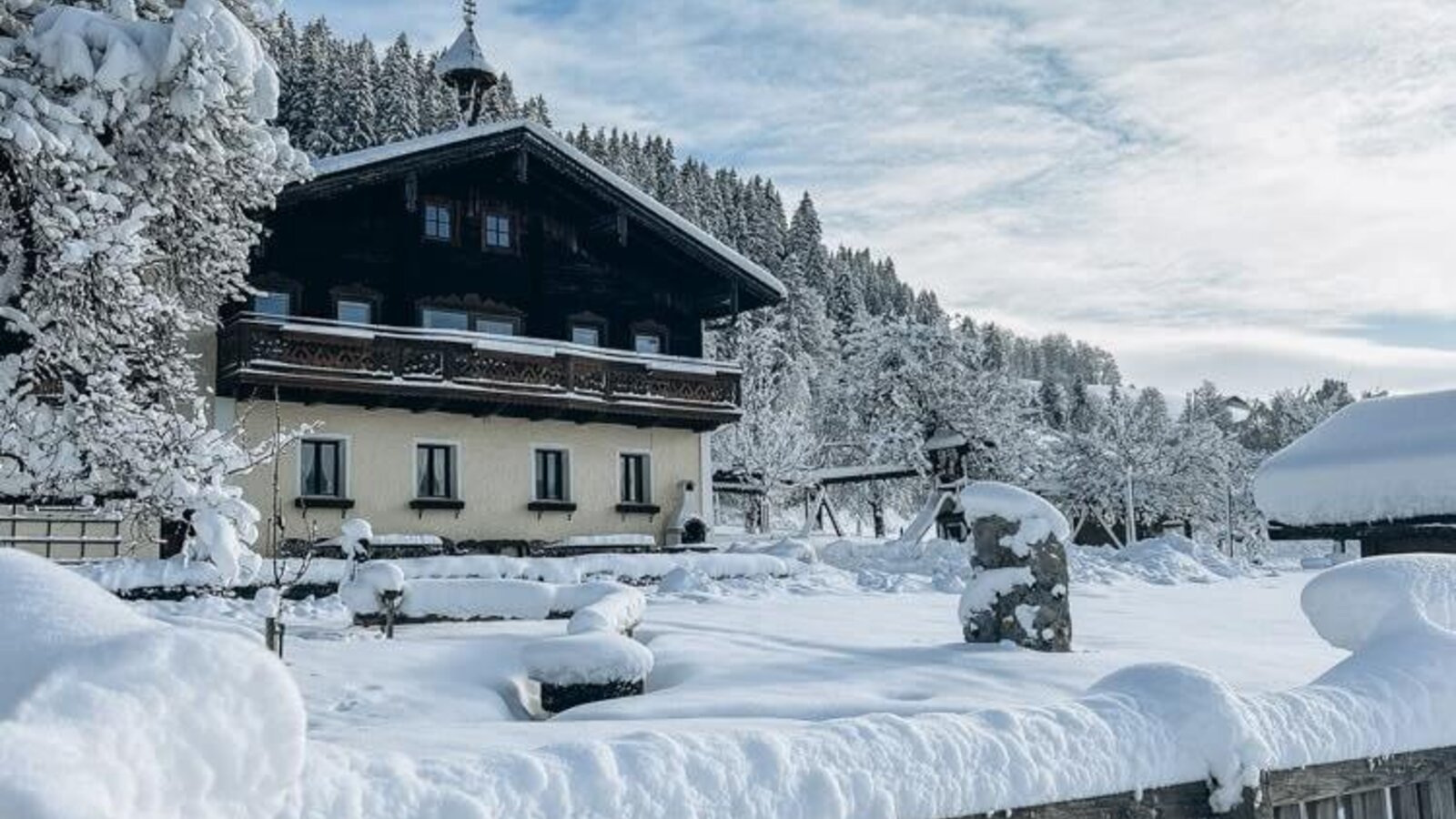 Der Bauernhof im Winter, umgeben von einer tief verschneiten Landschaft und Bäumen.