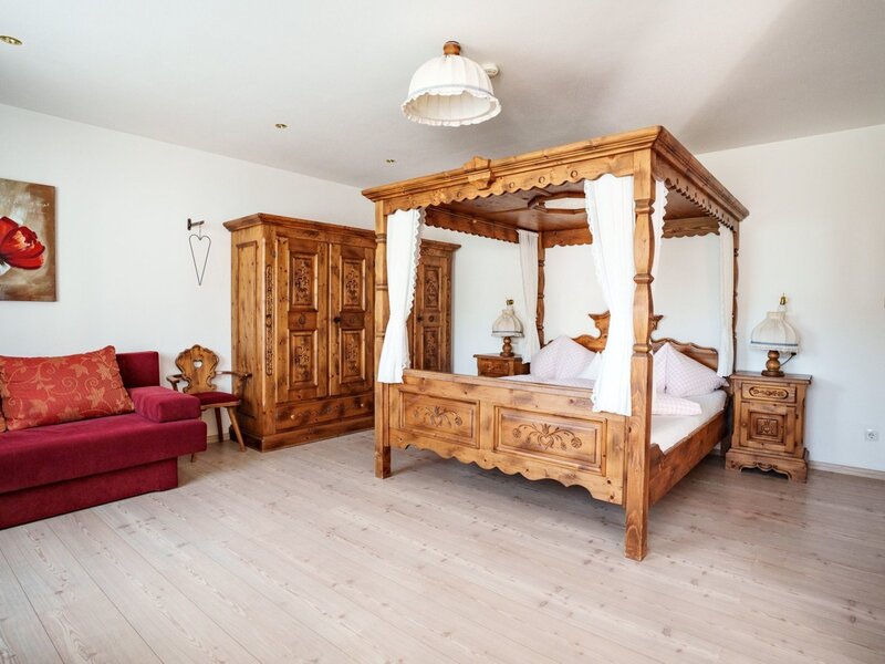 Schlafzimmer im Bauernhof mit Himmelbett, Holzschrank und rotem Sofa.