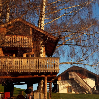 Das Baumhaus auf dem Bauernhof mit seinen Balkonen und einem Grillbereich, mit Blick auf die umliegende Landschaft und Berge.