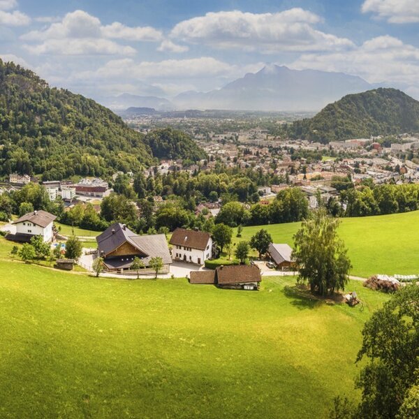 Malerischer Blick auf den Bauernhof, umgeben von grünen Wiesen und mit einer weitläufigen Aussicht auf die Stadt und Berge.