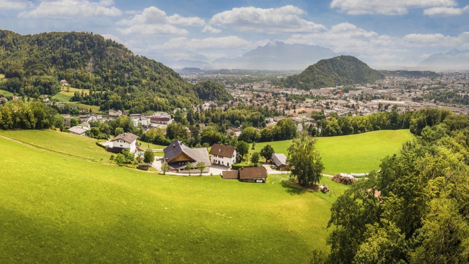 Malerischer Blick auf den Bauernhof, umgeben von grünen Wiesen und mit einer weitläufigen Aussicht auf die Stadt und Berge.