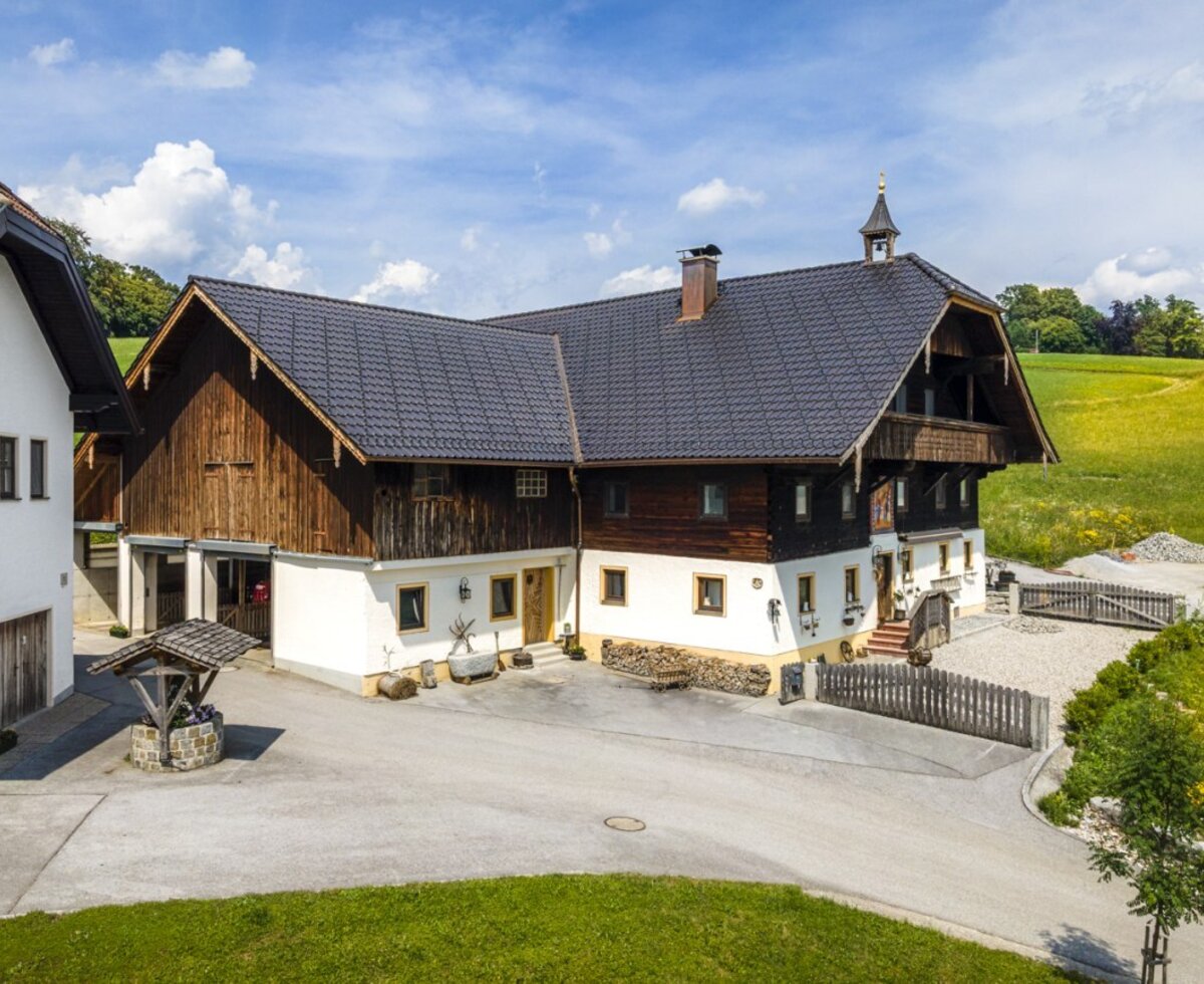 Der einladende Bauernhof mit seinem traditionellen Holz- und Steingebäude, umgeben von grünen Wiesen unter blauem Himmel.