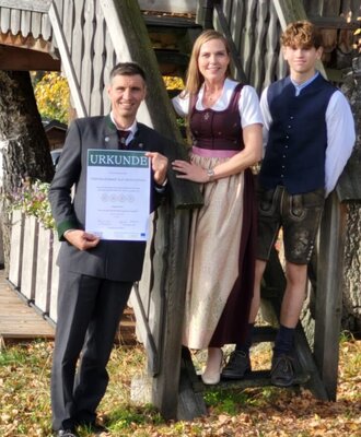 Die Gastgeberfamilie des Bauernhofs in Tracht präsentiert eine Auszeichnung.