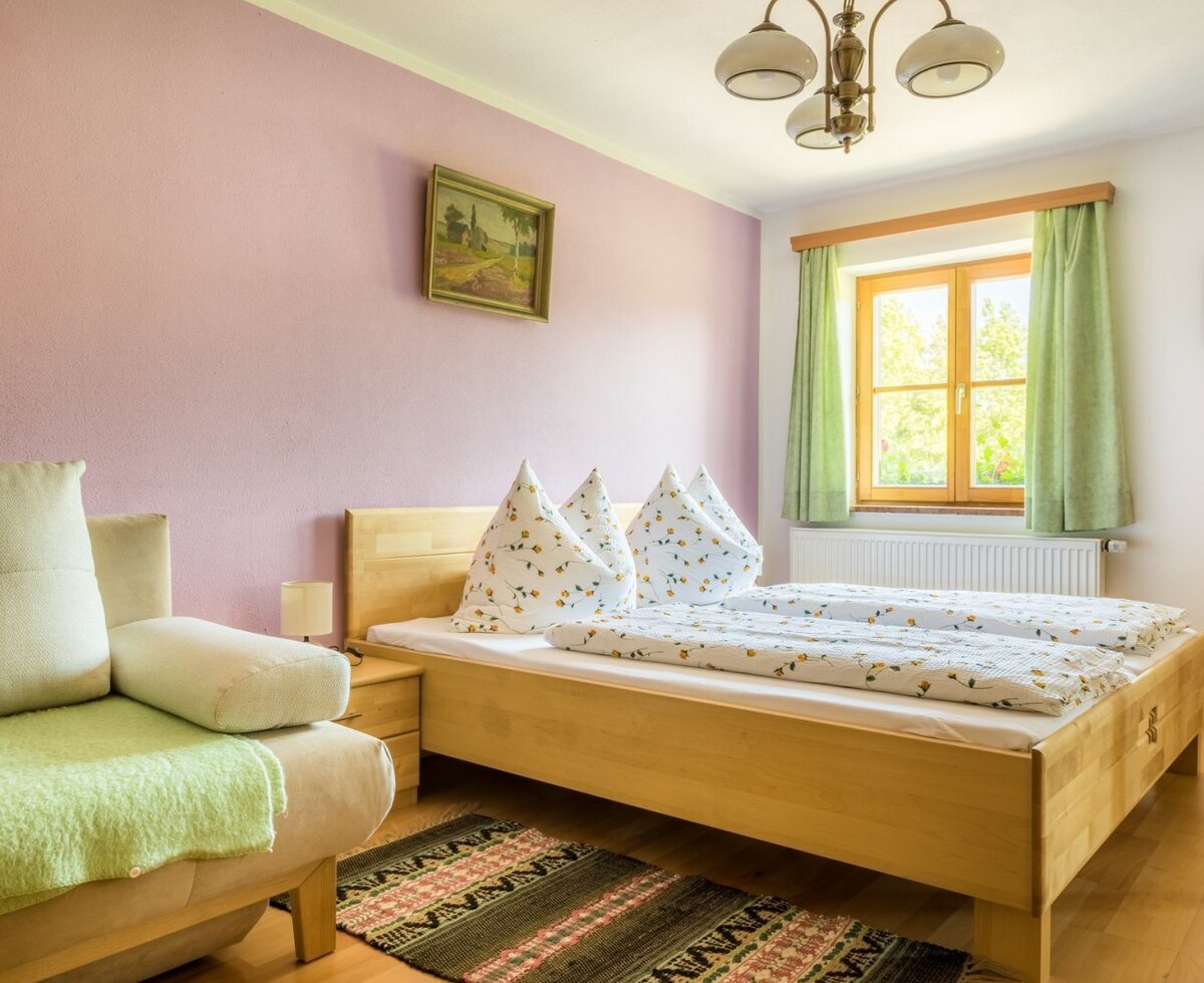 Schlafzimmer der Ferienwohnung auf dem Bauernhof mit Doppelbett, Schlafsofa, Holzboden und Fenster.