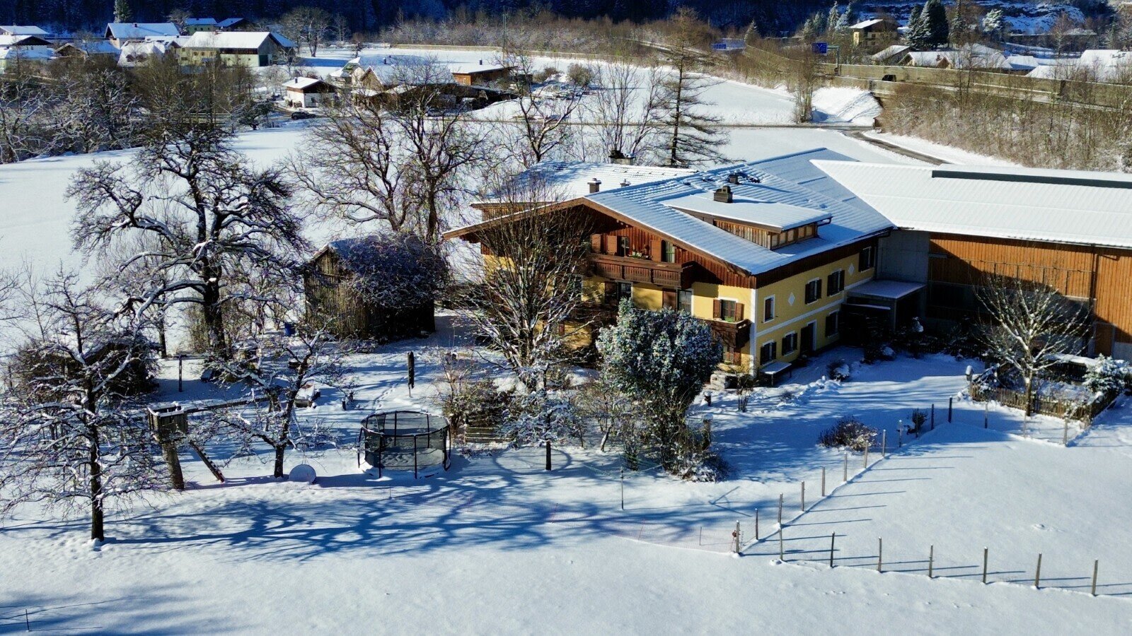 Außenansicht des Bauernhofs in einer verschneiten Landschaft mit Hauptgebäude und angrenzender Scheune.