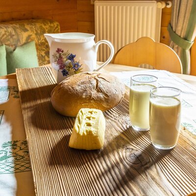 Brot, Butter und Milch auf einem Holzbrett, bereitgestellt für Gäste im Bauernhof.