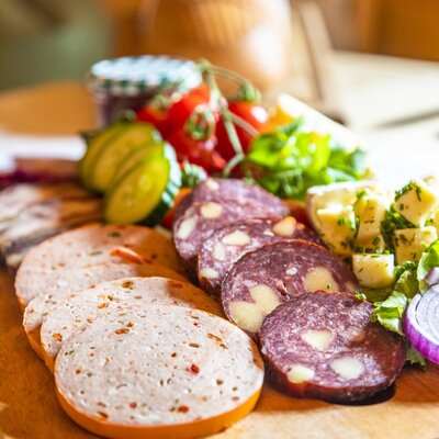 Eine Brotzeitplatte des Bauernhofs mit verschiedenen Wurst- und Käsesorten sowie frischem Gemüse.