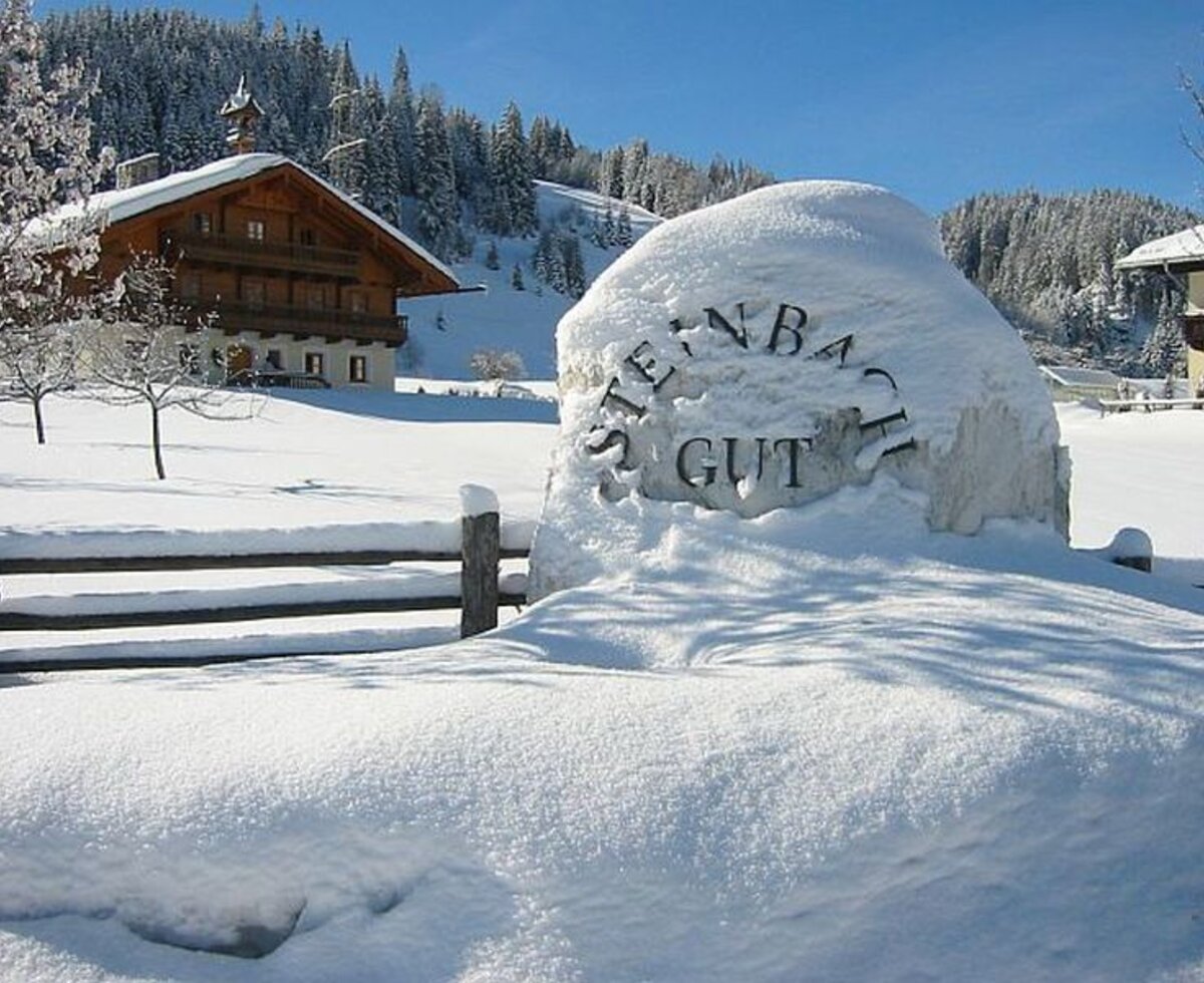 Winteransicht des Bauernhofs mit schneebedecktem Eingangsschild "STEINBACH GUT" und traditionellem Holzgebäude.