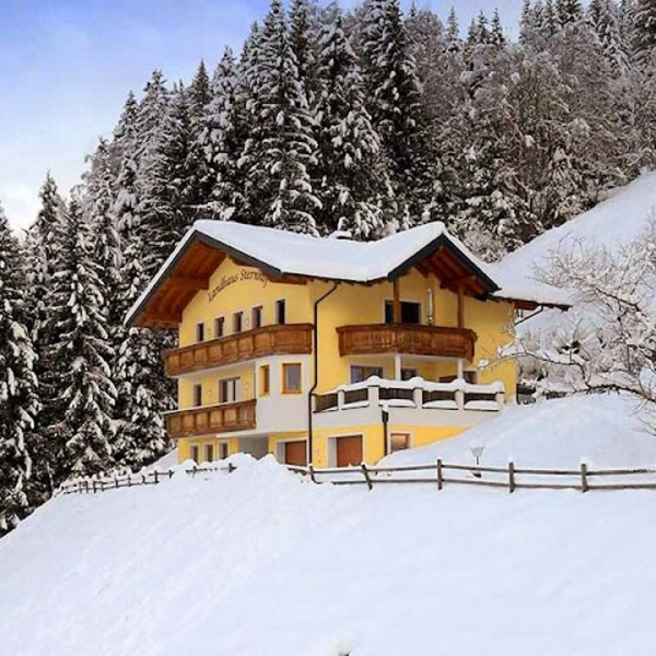 Außenansicht des Bauernhofs im Winter, umgeben von verschneiten Tannenbäumen und mit Balkonen.