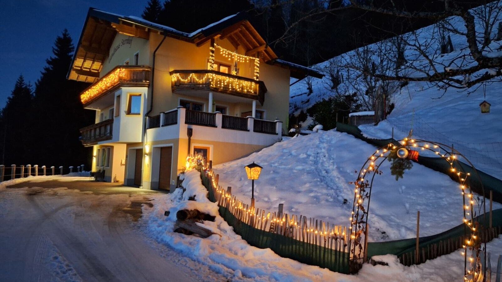 Der Bauernhof bei Nacht, festlich beleuchtet und von Schnee bedeckt.