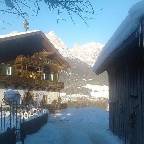 Der traditionelle Bauernhof mit Balkon und Blick auf die verschneite Berglandschaft.