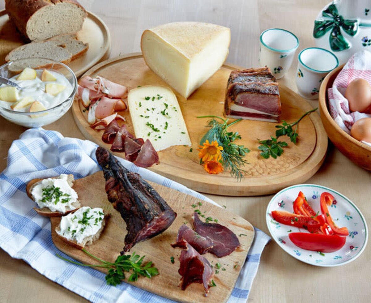 Eine Auswahl regionaler Produkte und Spezialitäten vom Bauernhof, darunter Brot, Käse, Wurst, Eier und Joghurt.