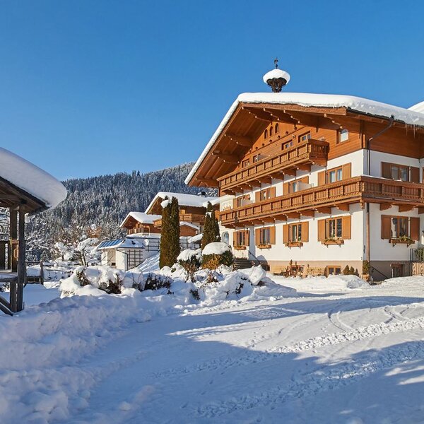 Der Bauernhof im Winter mit schneebedeckten Dächern und einem Holzpavillon auf dem Gelände.