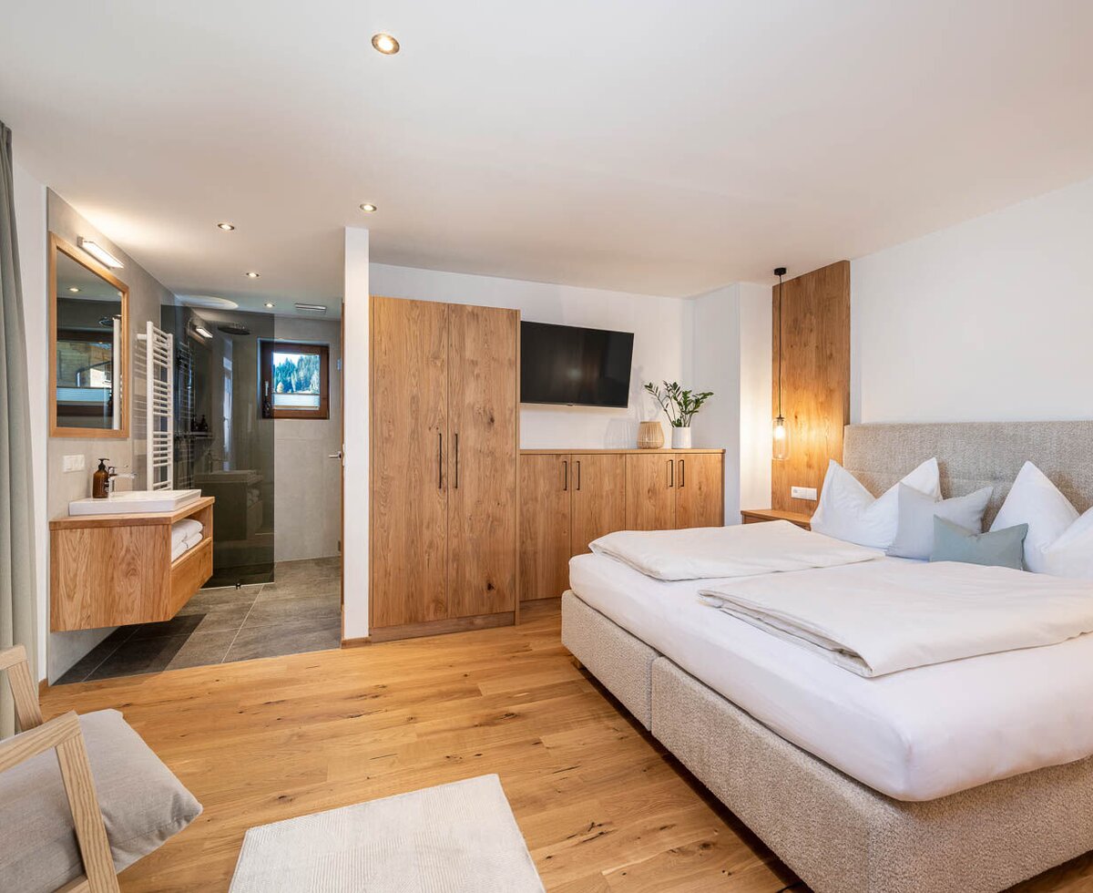 Schlafzimmer in der Ferienwohnung mit Doppelbett, Holzmöbeln, Fernseher und offenem Badbereich mit Dusche.