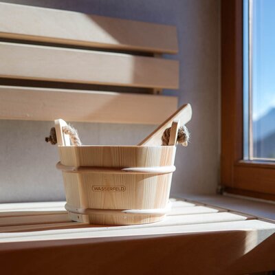 Hölzerner Saunaeimer mit Schöpfkelle in der Sauna des Bauernhofs, neben einem Fenster mit Bergblick.