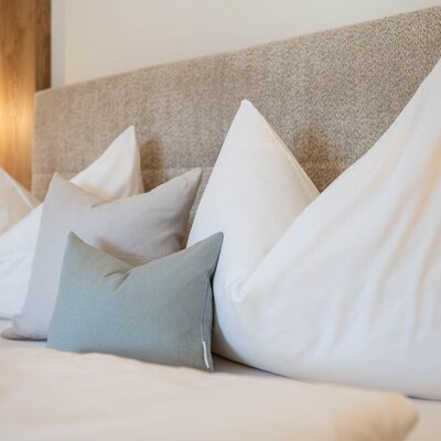 Schlafzimmer in einer Ferienwohnung des Bauernhofs mit Bett, gepolstertem Kopfteil, verschiedenen Kissen und Nachttischlampe.