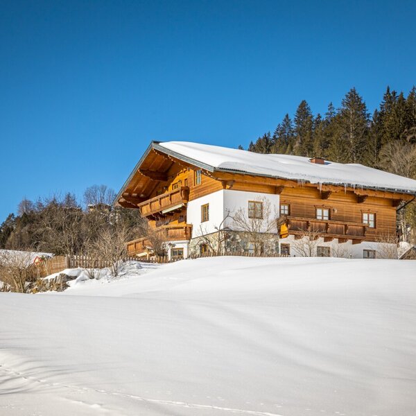 Die Außenansicht des Bauernhofs in sonniger, schneebedeckter Winterlandschaft.