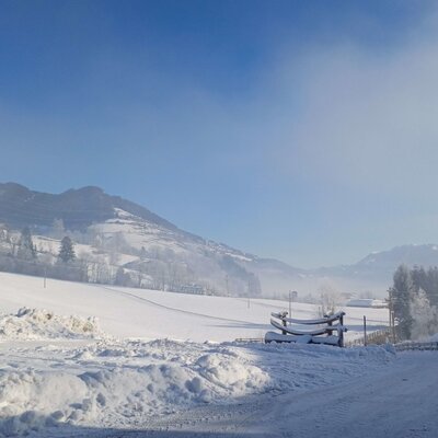 Winterlandschaft am Bauernhof mit schneebedeckten Feldern und Bergen.