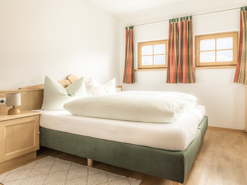 Doppelzimmer mit Doppelbett, Nachttisch und zwei Fenstern.