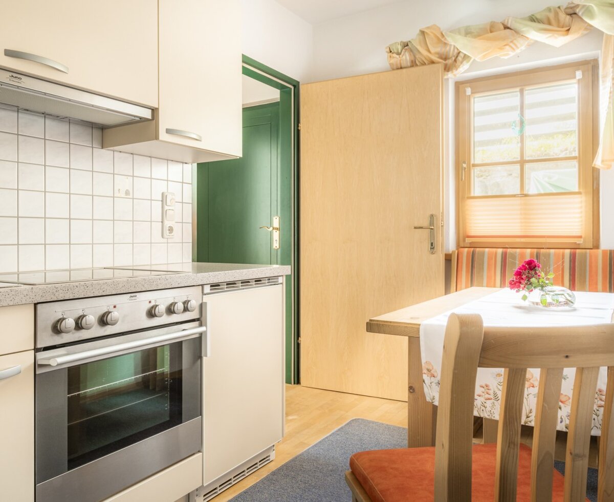 Die Küche , ausgestattet mit Backofen, Herd und einem Essbereich mit Holztisch und Sitzbank am Fenster.