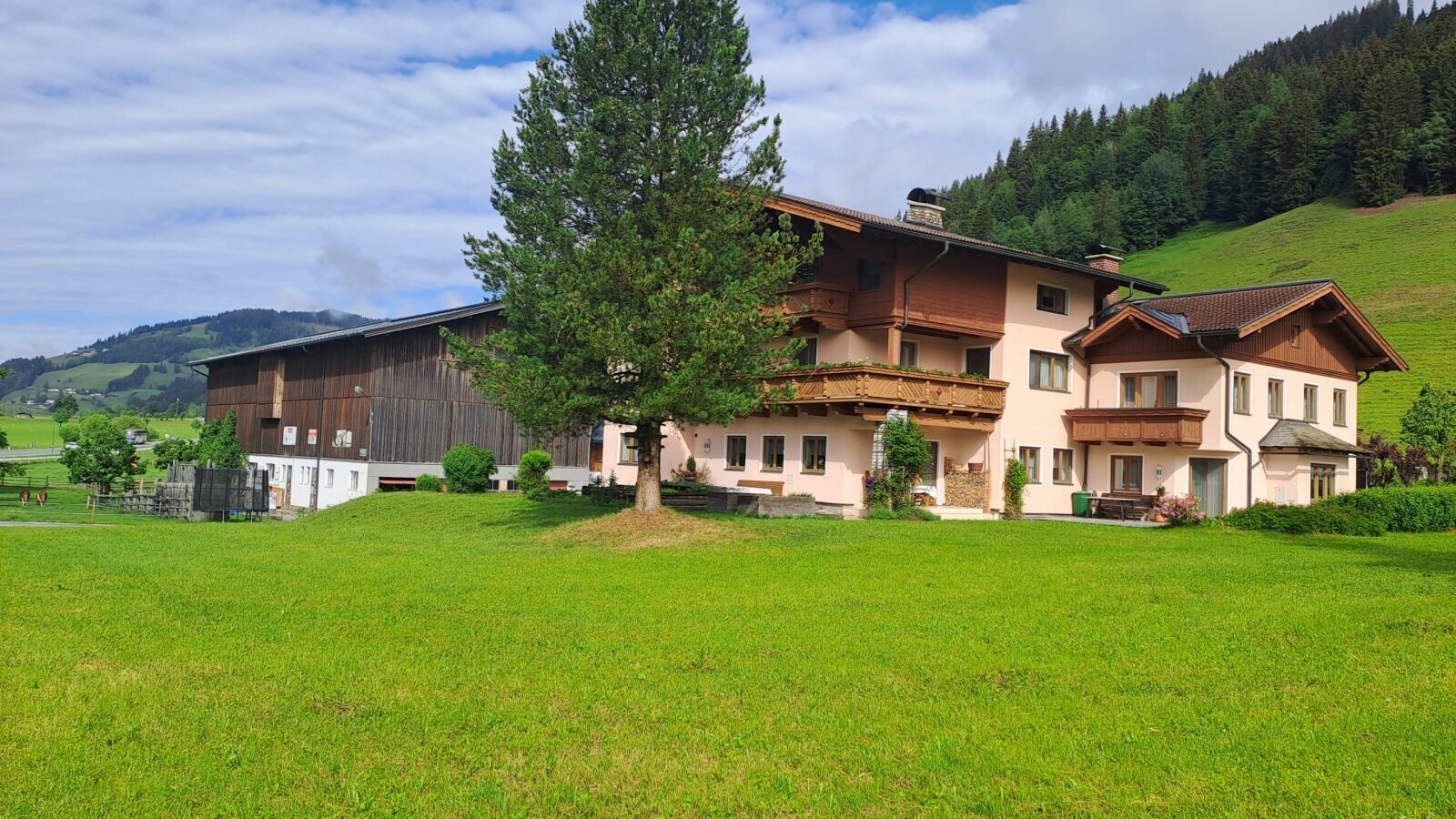 Außenansicht des Vierthalerhofs mit Balkonen, einer großen Rasenfläche und angrenzender Scheune vor einer Bergkulisse.