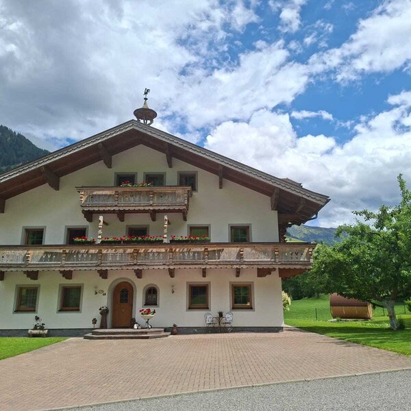 Der Voithof von außen, umgeben von Grünflächen und mit traditionellen Holzbalkonen sowie Bergblick.