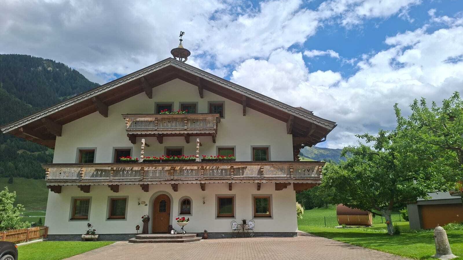 Der Voithof von außen, umgeben von Grünflächen und mit traditionellen Holzbalkonen sowie Bergblick.