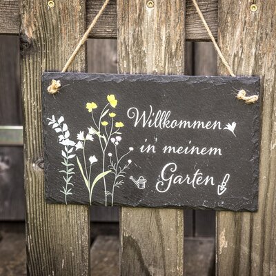 Ein charmantes Willkommensschild am rustikalen Holzzaun lädt Gäste in den Garten der Ferienwohnung ein.