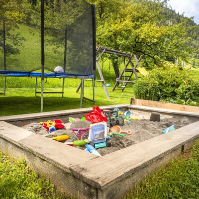 Der einladende Garten der Ferienwohnung mit einem vielseitigen Kinderspielbereich samt Sandkasten, Trampolin und Schaukel.
