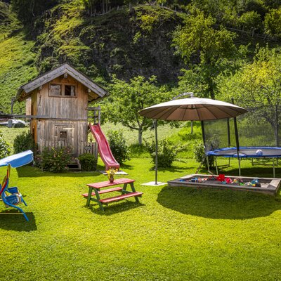 Der weitläufige Garten der Ferienwohnung bietet einen einladenden Kinderspielplatz mit Rutsche, Trampolin und Sandkasten inmitten grüner Natur.