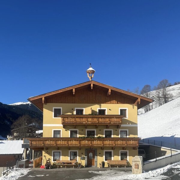 Außenansicht des Bauernhofs mit gelber Fassade, Holzbalkonen und schneebedeckter Landschaft.