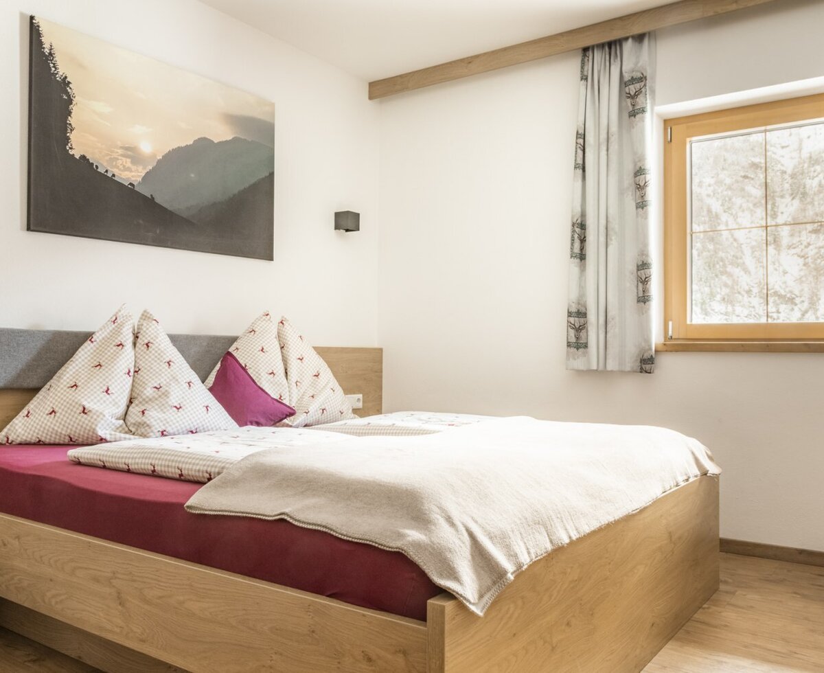 Schlafzimmer mit Doppelbett, Nachttisch und Fenster mit Vorhängen.