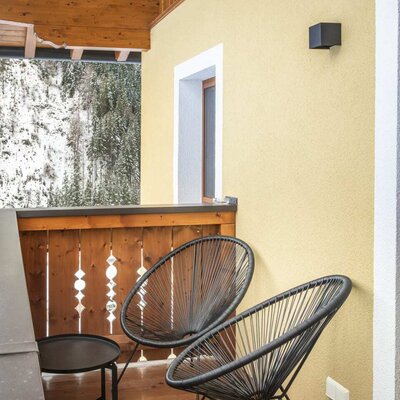 Balkon des Bauernhofs mit zwei Stühlen, einem Tisch und Blick auf verschneite Bäume.