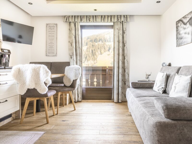 Wohnbereich der Ferienwohnung mit Sofa, Essbereich, Küchenzeile, TV und Zugang zum Balkon mit Bergblick.
