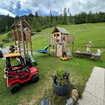 Der Kinderspielplatz der Ferienwohnung bietet Holzspielgeräte, Schaukeln, eine Rutsche und ein Spielhaus.